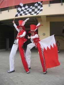 Flag waving stilt walkers for hire. Our Checkered Cyclist Stilt Walkers are available to book for summer festivals in London & the UK.