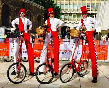 Checkered Cyclist Stilt Walkers for hire. Our comedy cycling stilt walkers are available to book for family fun days, Easter events or shopping centre events in London & the UK.