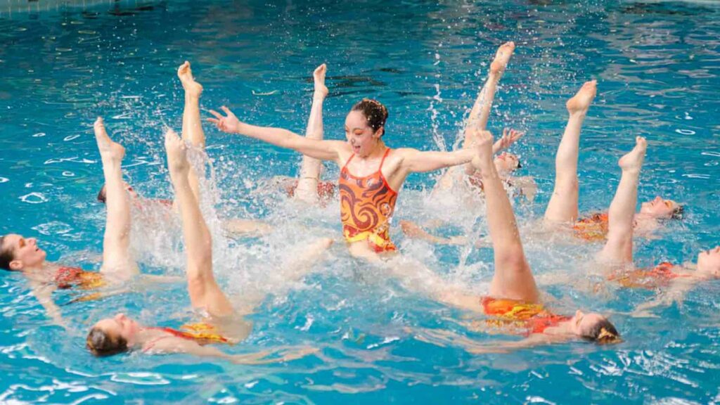 synchronised swimmers performers in a pool upside down in orange leotards