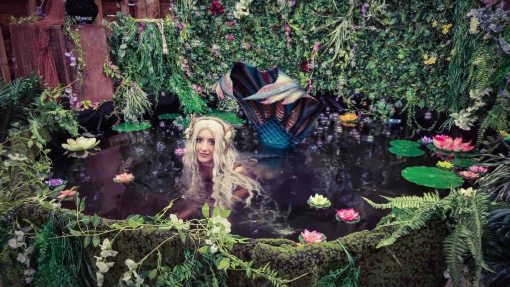 A stunning professional realistic mermaid for hire poses from her lagoon style pool