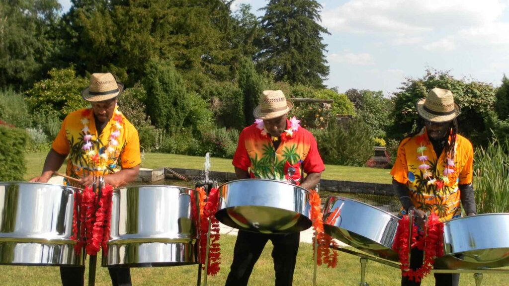 Three steel drummers in vibrant shirts playing at an outdoor event.
