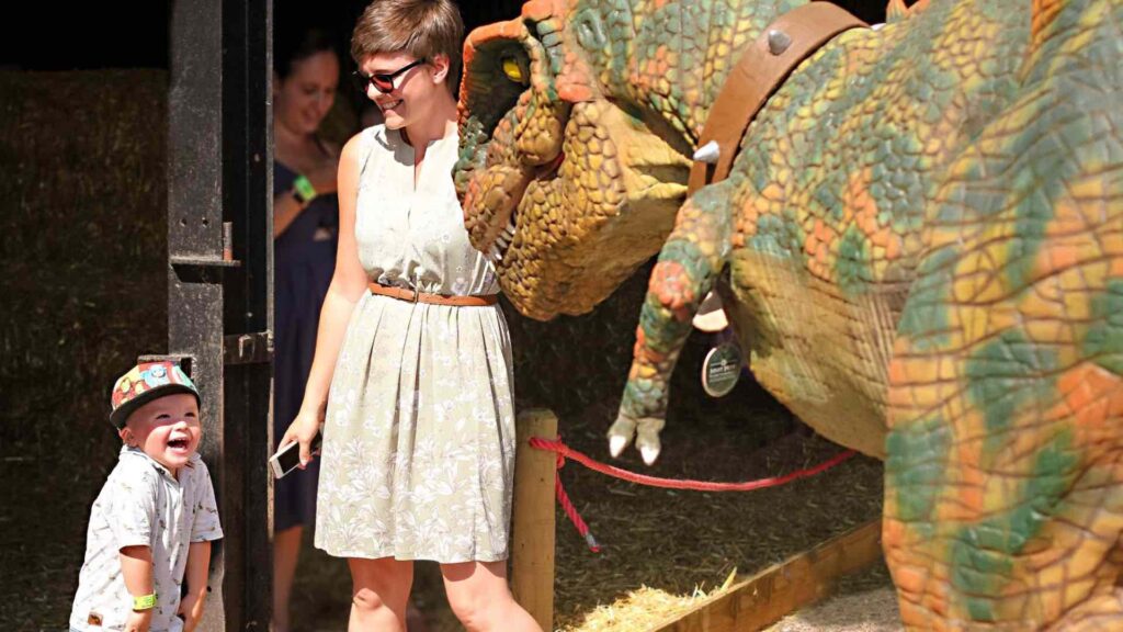 a walkabout dinosaur sniffs a lady in a white dress