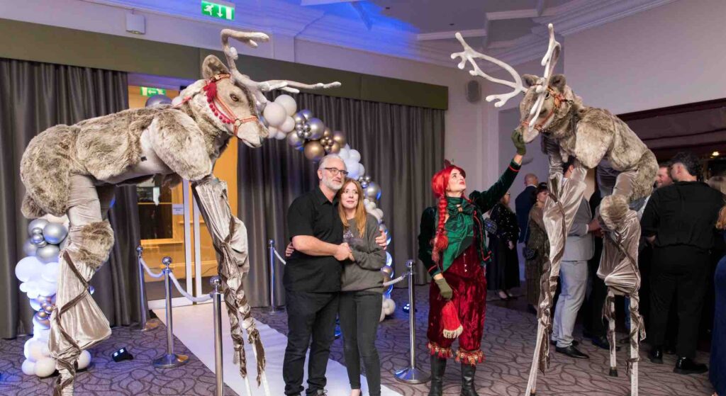 Guest posing with Reindeer stilt walkers at a Christmas event.