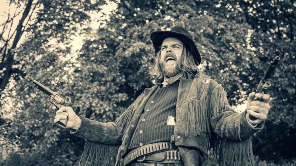 Gunslinger performer screaming and shooting guns at wild west party.