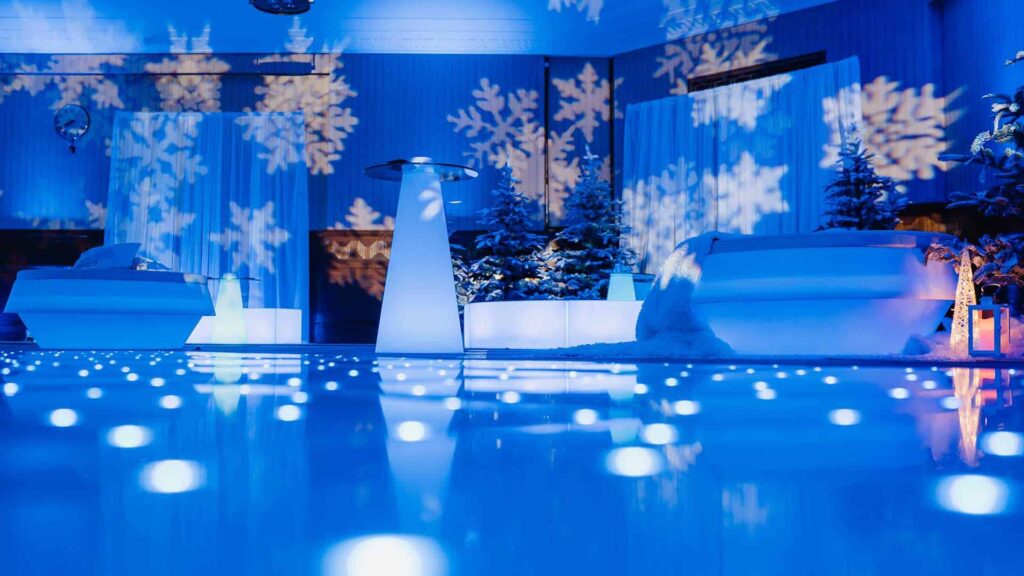 Various decorations including snowflake projections, Christmas trees covered in snow and draping used to dress venue space in winter wonderland theming