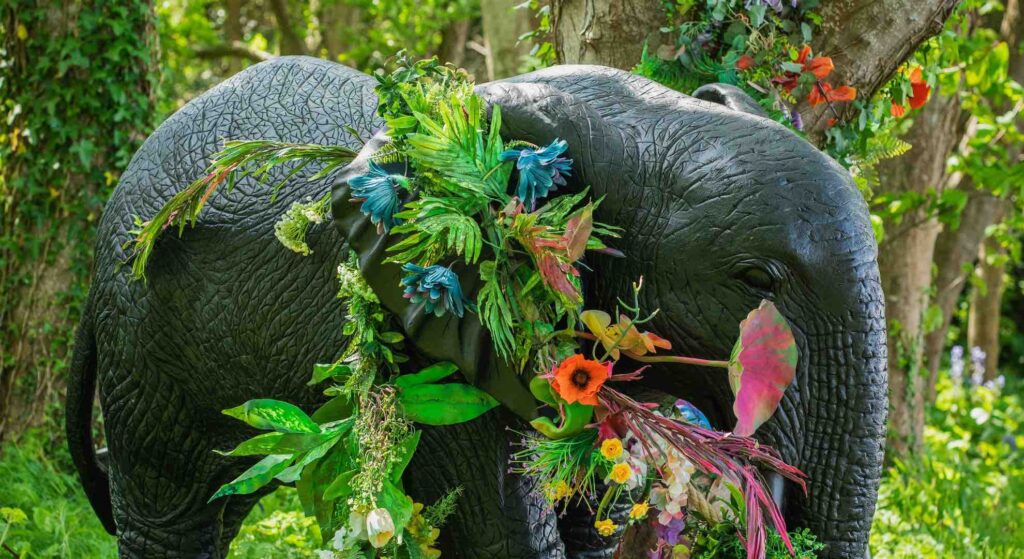 Giant elephant prop wrapped in vibrant floral decoration at jungle themed event.