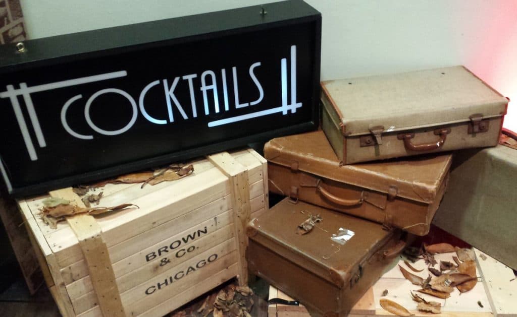 1920s themed cocktail sign stacked on vintage style suitcases used as part 0f 1920s prohibition and Gatsby props for venue dressing.