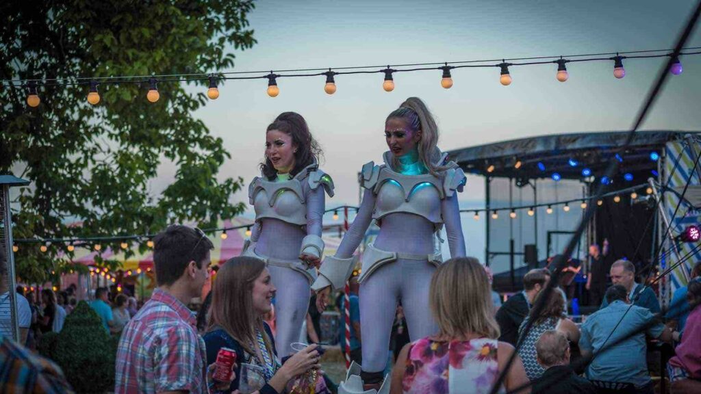 Stilt walking performers wearing light-up costumes walking through crowds