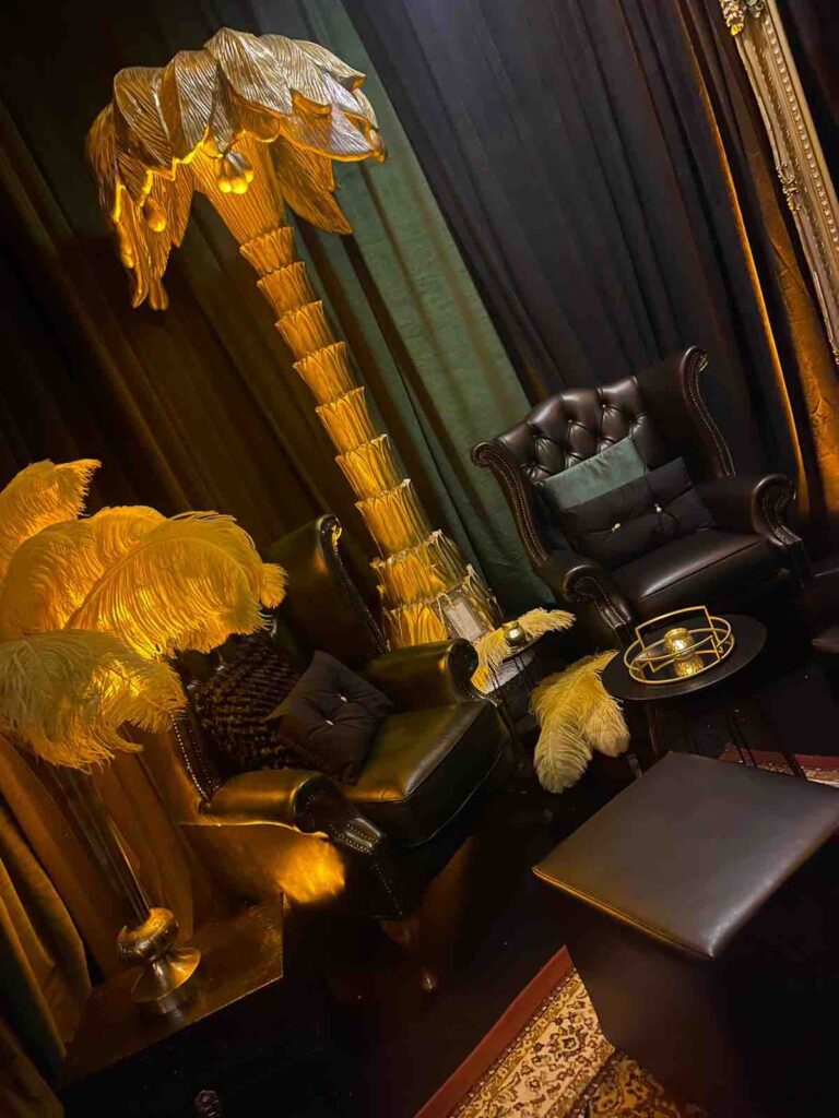Giant 1920s style gold palm tree prop, leather armchair and ostrich feathers used to decorate 1920s themed room at event.