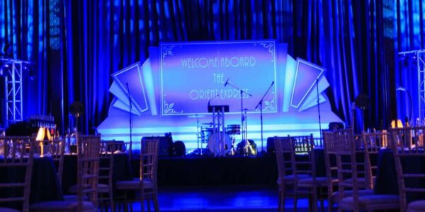 Stage decorated with 1920s inspired backdrop and lit up with blue lighting great for 1920s orient express themed event.