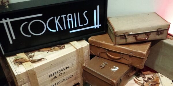 1920s themed cocktail sign stacked on vintage style suitcases used as part 0f 1920s prohibition and Gatsby props for venue dressing.