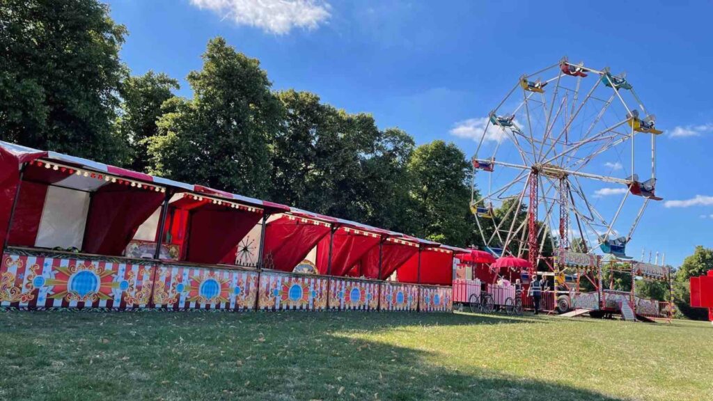 Row of fair ground gaming stalls set-up at outdoor venue next to ferris wheel