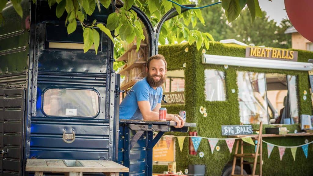 Food vendor leaning out of food truck and smiling at camera at festival themed event