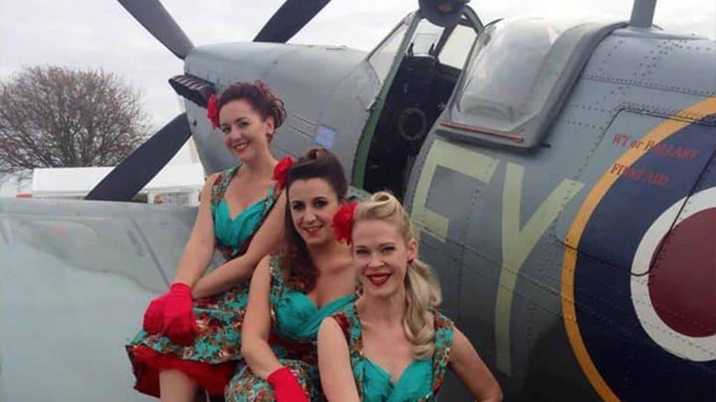 Vintage 1940s style girl group posing whilst sitting on spitfire plane
