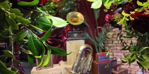 1920s themed musical event props installation including brass instruments and gramophone behind some flowers at a prohibition themed event.