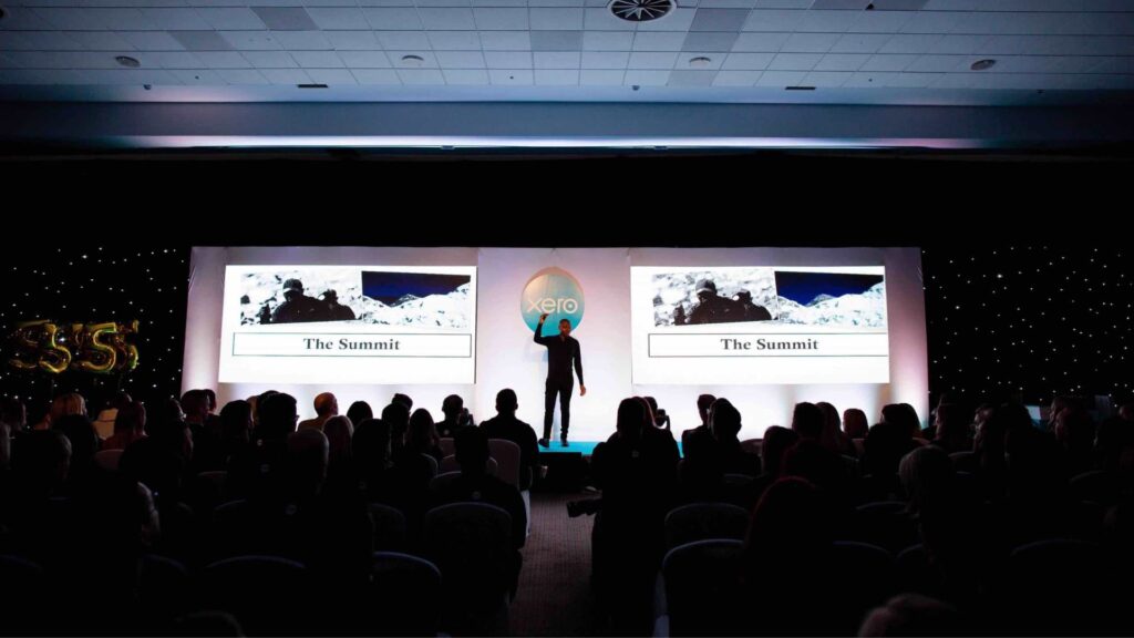 War Veteran and Keynote Speaker, Ben McBean on conference stage delivering talk on 'the summit'.