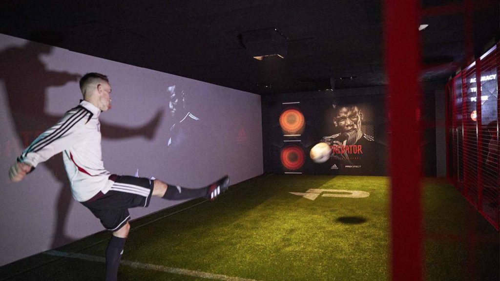 Man in full football kit kicking football into penalty shoot out board. Football themed props available to hire London UK