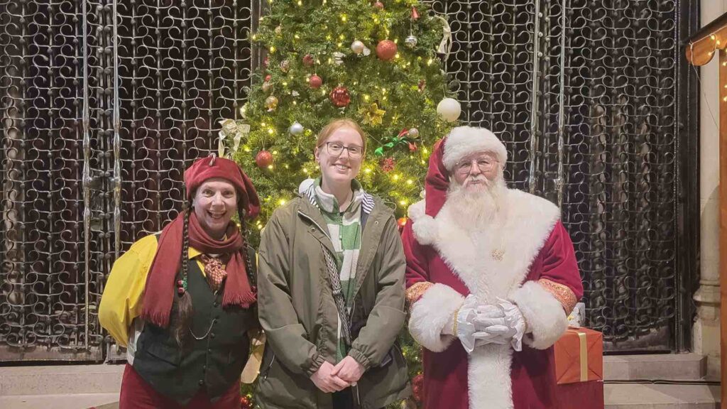 Eden our event manager with Santa claus performer and an elf with Christmas tree in the background at Hampshire.