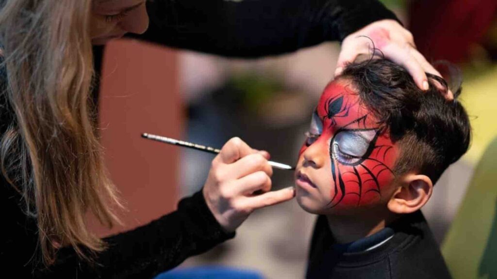 Experienced face painter painting Spider-Man design on child's face at face painting pop-up area.