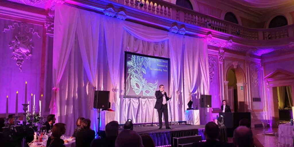 Host on stage presenting awards to staff in audience at a Award and Gala Dinner event.