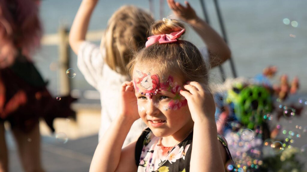 Company family fun day girl with face painted playing with bubbles at an event.