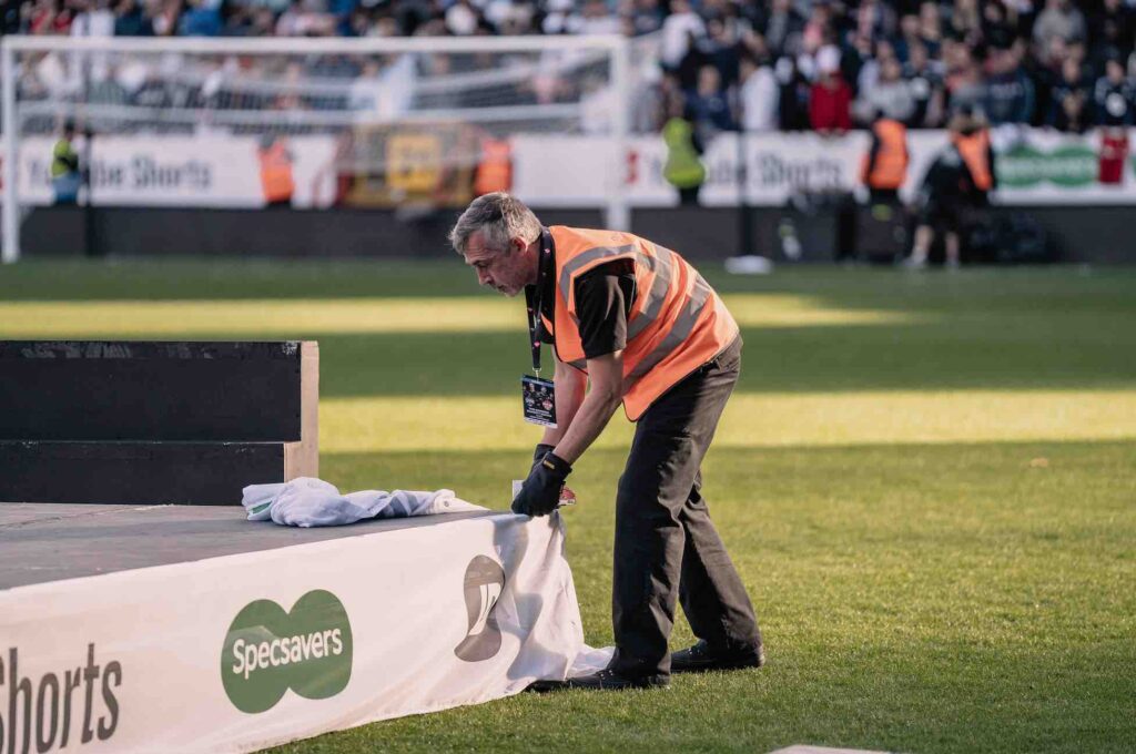 Team adding branded elements to stage on pitch at football match.