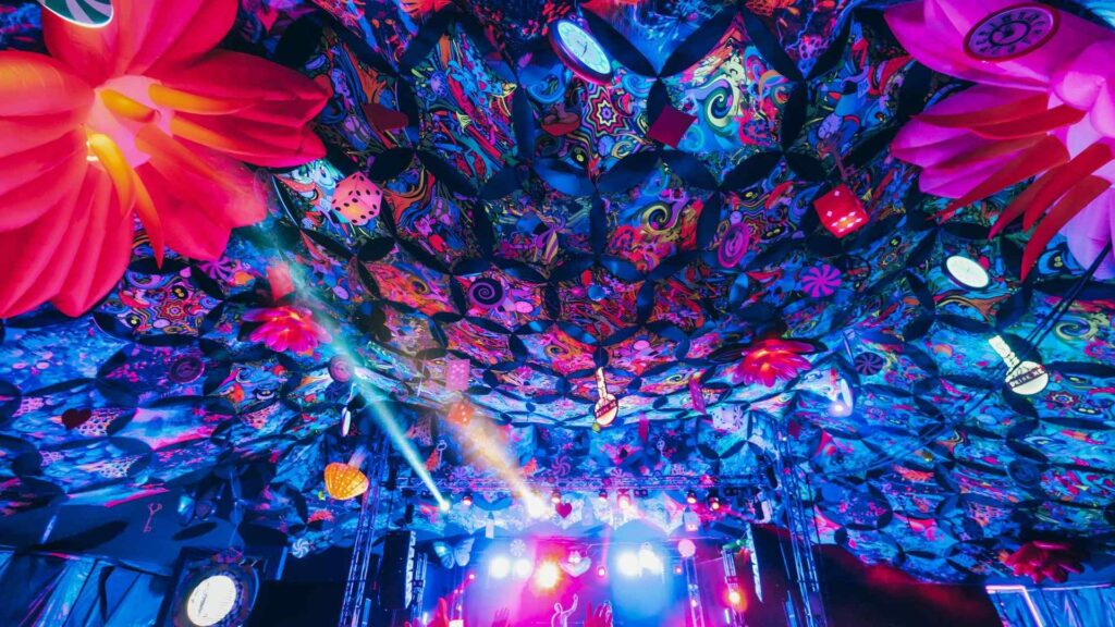 Blue, purple and red patterned ceiling canopy in front of stage and set at festival event at night.