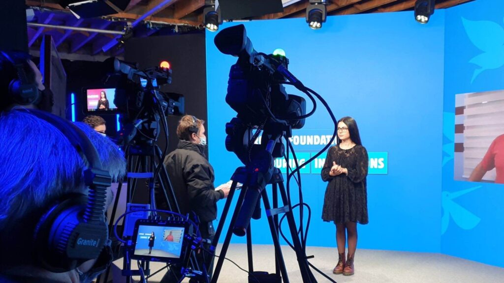 Presenter on studio stage talking to virtual audience.