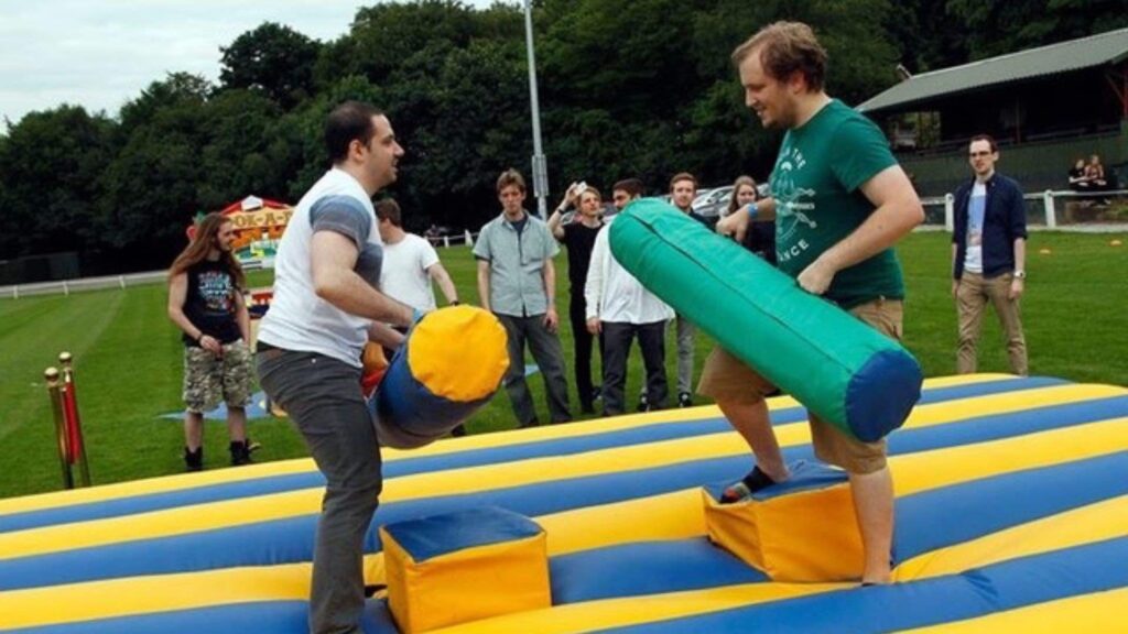 Two people holding inflatable logs trying to push each other off podiums in team building challenge