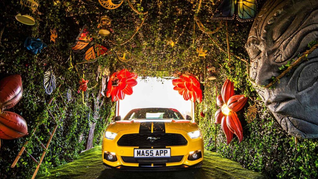Yellow convertible ford mustang in nature and tiki themed tunnel for brand activation.