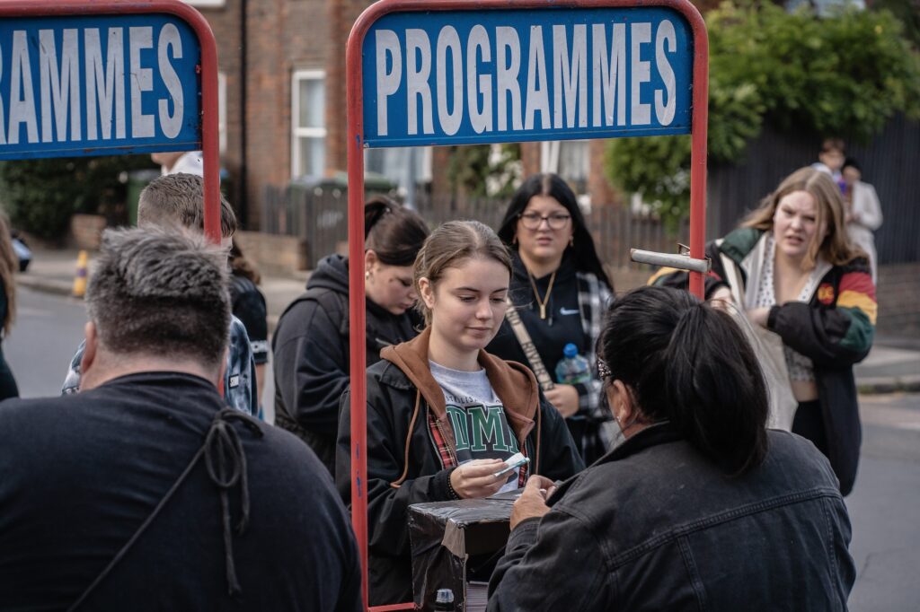 Girl buying programme at stand at fan zone football match event.