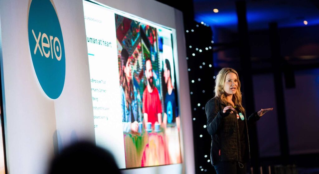 Female guest speaker called Rachel on stage motivating XERO employees hired by our conference company.