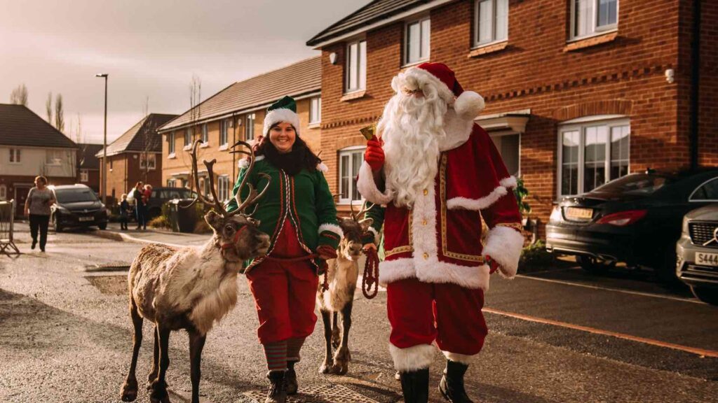 Elf and Santa walking through village with reindeer
