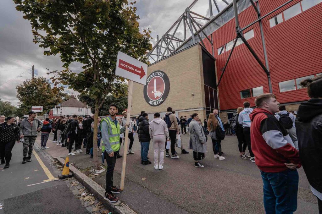 Man in high vis holding sign pointing crowds in the right direction outside Charlton Athletic football stadium.