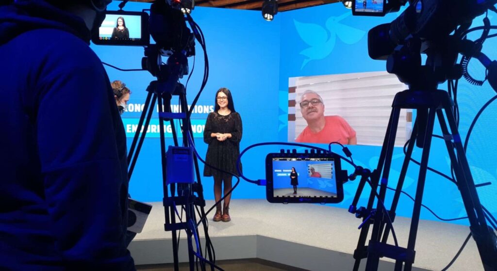 Woman stood in front of camera on stage for virtual conference.