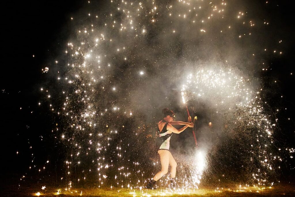 Female fire dancer wearing sequin playsuit twisting fire sparklers around her body as part of her fire dancing performance for a festival themed party.