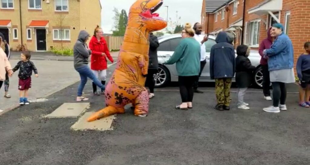 Tenant in a T-Rex costume lined up to collect her ice cream at simple life ice cream community event.