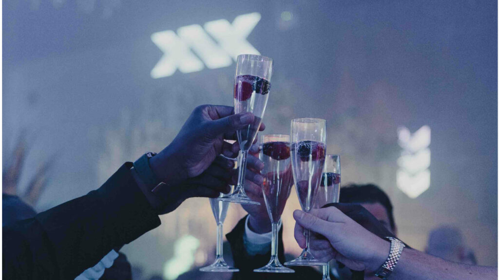 Guests at XIX product launch party holding up champagne glasses in front of XIX Vodka bespoke sign.