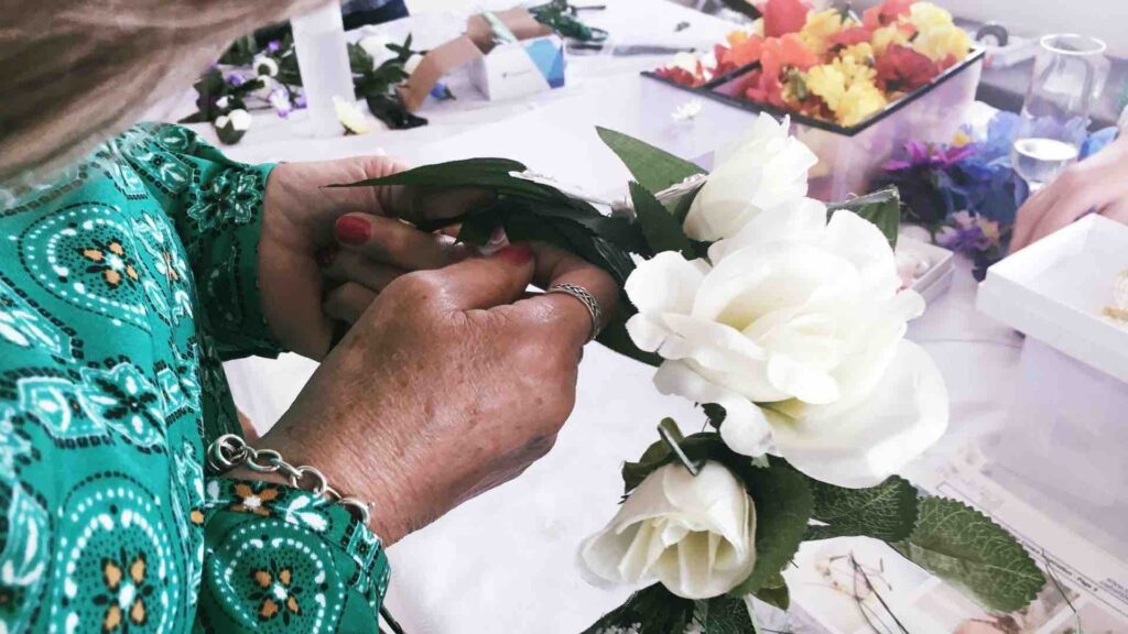 Person using white flowers to decorate wreath