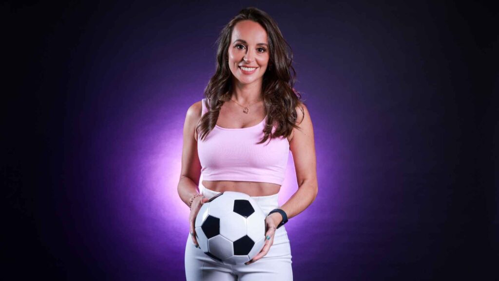 A female football freestyler posing for a press shot with a football.