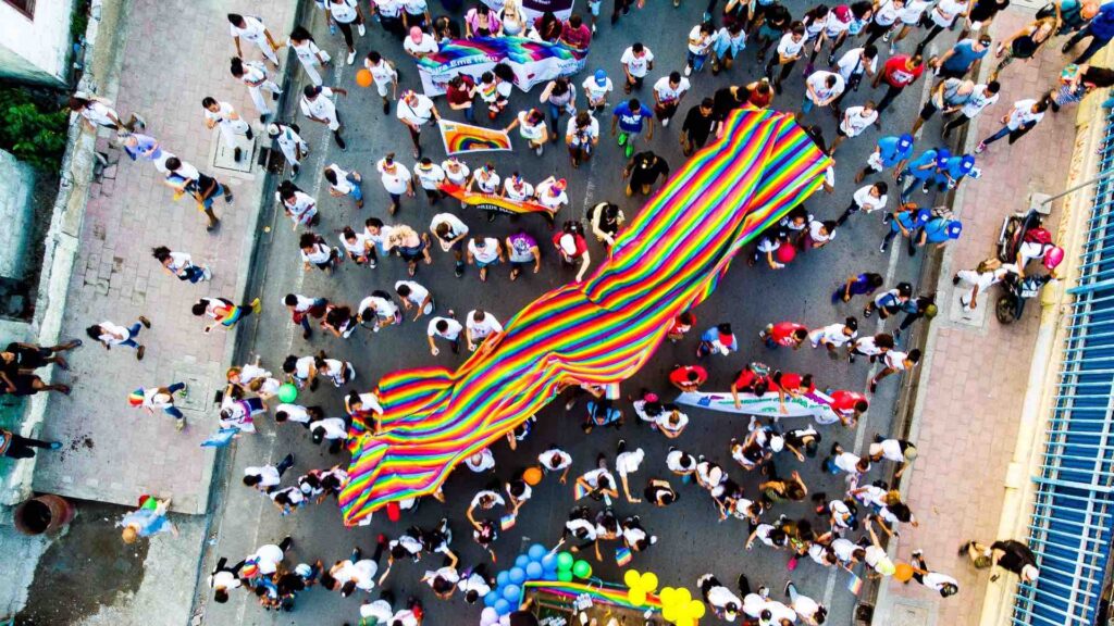 Pride celebration aerial view with groups of people holding rainbow flags and banners.
