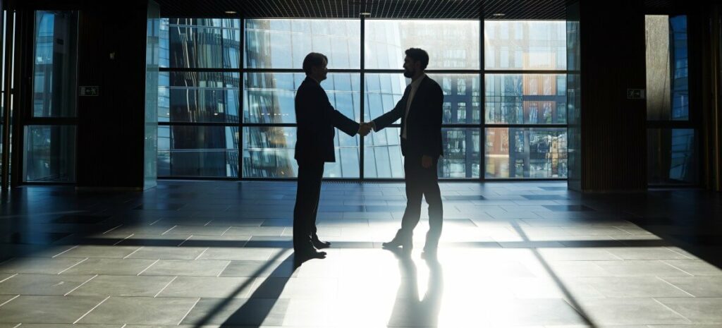 2 people shaking hands in front of glass window after agreeing a contract to work in Saudi Arabia.