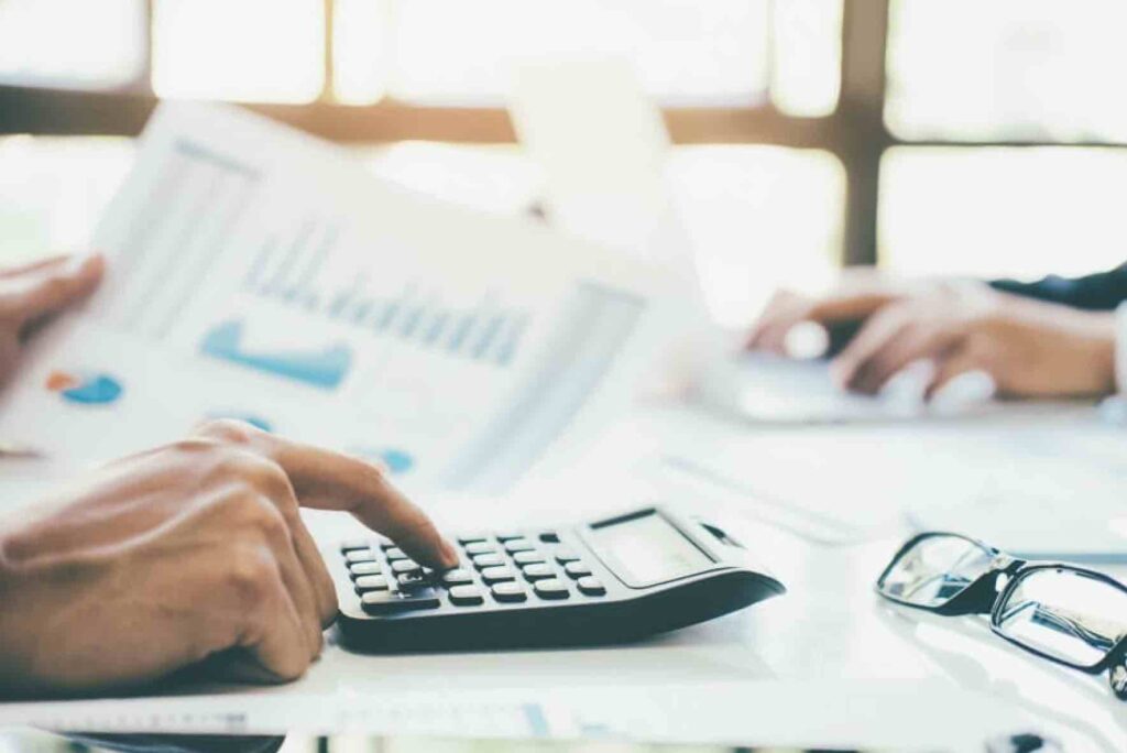 Conference manager working out a budget for conference by typing numbers into calculator.