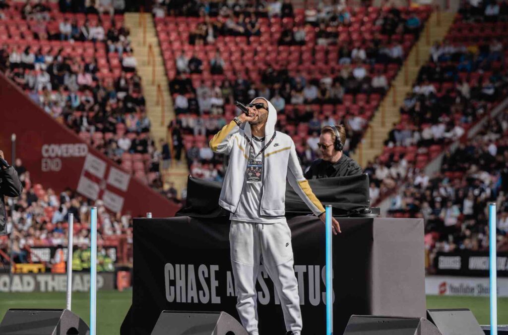Chase and status perform on stage at charity football match, booked through influencer event services.