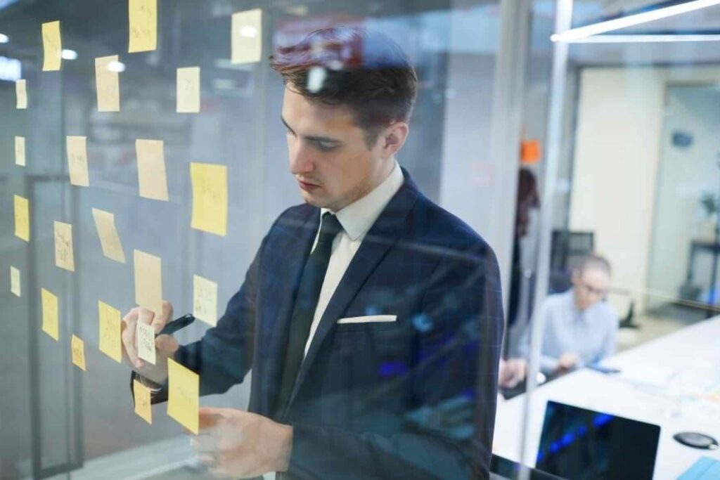 Man sticking yellow sticky notes onto wall and making notes.