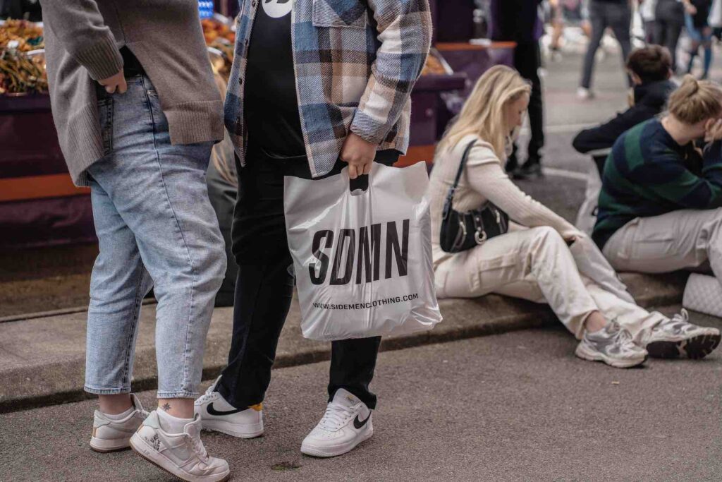 Sidemen branded shopping bag held by fan attending YouTube and Sidemen charity football match.
