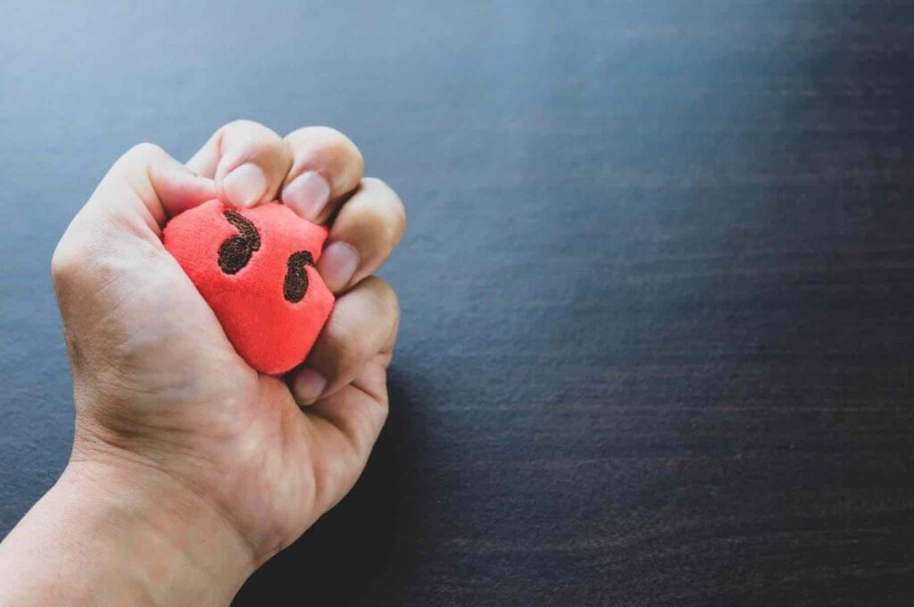 Person gripping red stress ball with an angry face.