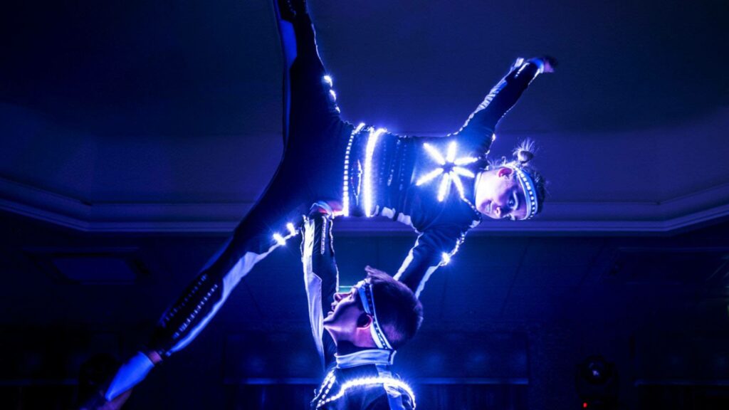 Woman balancing on top of acrobatic duo partner in LED suit