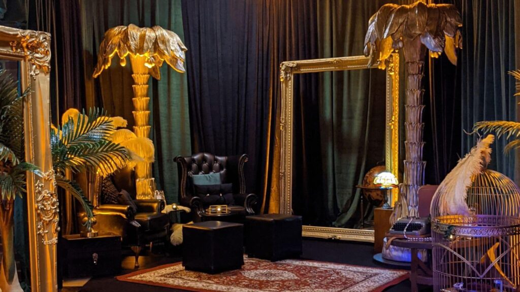 Luxury black and gold themed lounge with large mirrors, palm trees and armchair.