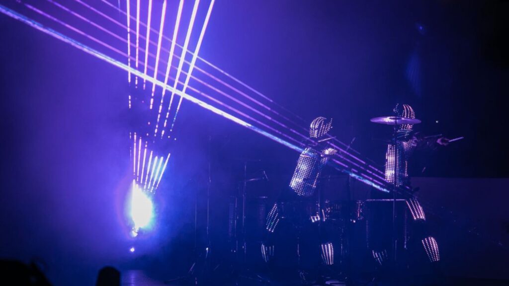 a crowd cheers on glowing LED drummers who are dancing in rhythm to club hits